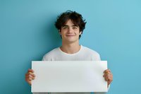 Young Hispanic man with curly dark hair wearing white sweater holds blank white horizontal banner against blue background, smiling warmly at camera.