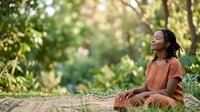 Young woman of African descent sitting outdoors in natural woodland setting, wearing casual terracotta shirt, relaxed pose on ground with lush green foliage background, suitable for lifestyle and wellness content.