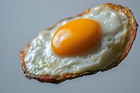 Close-up macro shot of sunny side up fried egg with crispy brown edges and bright orange yolk on gray background, showing texture and details of cooking.