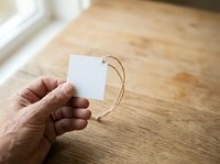 Caucasian male hand holding blank white price tag with twine on wooden floor background, suitable for retail, pricing, and product labeling concepts.
