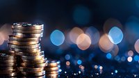 Stack of silver and gold coins on dark background with blue bokeh lights creating financial atmosphere. Money savings concept for banking and investment.