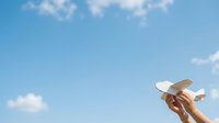 Woman's hand holding white sun hat against blue sky with clouds, summer travel and vacation concept.