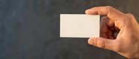 Hand holding a blank white business card against a dark textured background, copy space for branding, contact details, or logo mockup design.
