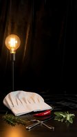White chef hat with kitchen utensils and herbs on dark wooden surface under warm Edison bulb lighting for culinary cooking concepts.