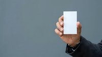Male hand holding blank white card against gray background, suitable for business card mockups, branding presentations, and marketing materials.