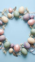 Pastel colored Easter eggs arranged in circular frame with dried flowers and feathers on soft blue background for spring holiday celebration and greeting cards.