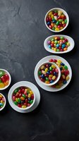 Colorful candy assortment in white bowls on dark slate background for party treats and confectionery displays.