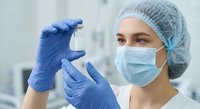 Female healthcare professional in protective equipment examining medical vial in laboratory setting for pharmaceutical research and development.