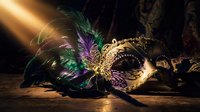 Ornate carnival mask with colorful feathers and golden details on wooden surface with dramatic lighting for masquerade party celebration events.
