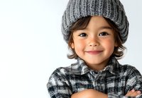 Young Asian child wearing gray knit beanie and plaid flannel shirt smiles warmly with arms crossed against white background, expressing joy and confidence.
