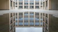 Modern residential or office building courtyard with symmetrical architecture, concrete facades, and large windows reflecting sky, suitable for corporate, real estate, and urban design projects.