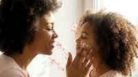 Young African American mother and daughter with curly hair bonding together near window with pink flowers, showing love and affection.