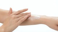 Woman applying moisturizing cream or lotion on arm skin against white background. Skincare, cosmetics, beauty treatment, dermatology concept for commercial use.
