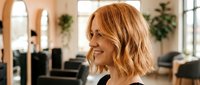 Young blonde woman with wavy bob haircut smiling in modern office workspace. Professional businesswoman portrait for corporate communications and workplace content.