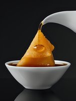 Poached pear in syrup with dramatic lighting against dark background, golden fruit floating in white ceramic bowl with rich brown liquid.