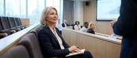 Confident mature businesswoman smiling during corporate presentation in modern conference room with colleagues in background.