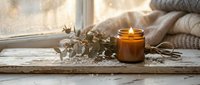 Cozy home interior with burning candle, eucalyptus branches and knitted blanket on wooden windowsill creating warm hygge atmosphere for relaxation and comfort.