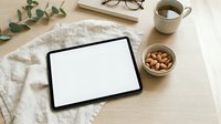 Digital tablet with blank white screen on wooden desk workspace with coffee cup, nuts, eucalyptus branch and eyeglasses for mockup presentations.