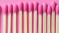 Row of pink cotton swabs arranged in neat line on matching background for medical hygiene and beauty care applications.