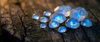 Blue opal gemstones scattered on weathered wooden surface with natural lighting creating magical sparkle and iridescent glow for jewelry design.