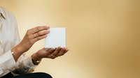 Hands holding blank white card on warm beige background, ideal for business cards, invitations, or promotional materials.