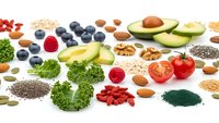 Healthy superfood ingredients including avocado, berries, nuts, seeds and vegetables arranged on white background for nutritious meal planning.