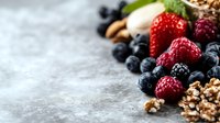 Fresh berries and granola scattered on gray stone background with copy space. Healthy breakfast ingredients for natural eating and clean diet.