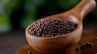 Fresh black peppercorns in wooden spoon on dark rustic background with selective focus. Natural spices and seasonings for cooking and food preparation.