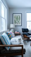 Modern living room with gray sofa, white cat, botanical fern artwork, black leather chair, and bright windows for home decor and interior design projects.