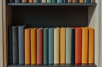Colorful hardcover books arranged on dark wooden shelf in muted vintage tones of orange, teal, and gray, creating minimalist library aesthetic for home decor.