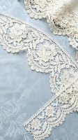 Delicate cream lace trim with intricate floral patterns on soft blue fabric background for vintage wedding dress sewing crafts and romantic textile projects.