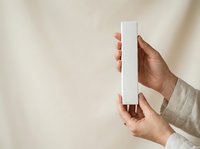 Close-up of hands holding blank white rectangular box against neutral background. Suitable for product packaging mockups, branding presentations, and commercial advertising campaigns.