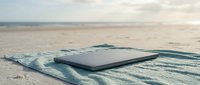 Laptop computer on striped beach towel in sand by ocean, representing remote work, digital nomad lifestyle, and summer productivity near water.