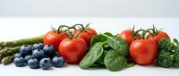 Fresh organic vegetables and berries arranged on white background including tomatoes, asparagus, blueberries, spinach and broccoli for healthy eating.