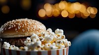 Fresh hamburger with popcorn against blurred bokeh lights background, creative movie night food concept for entertainment and cinema snacks.