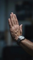 Mature male hand raised in stop gesture wearing metallic wristwatch against blurred urban background. Suitable for concepts of refusal, halt, rejection, authority, and time management.