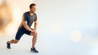 Athletic Caucasian man in blue sportswear performing dynamic lunge exercise outdoors during golden hour workout session for fitness and health training.