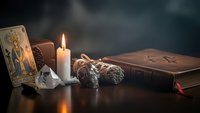Mystical tarot cards with burning candle, sage bundle and crystals on dark wooden table creating atmospheric fortune telling scene for spiritual guidance.