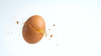 Cracked brown chicken egg with golden yolk spilling out and scattered eggshell pieces on clean white background for cooking and breakfast concepts.