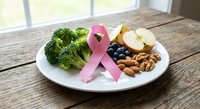 Pink ribbon with healthy foods broccoli apple nuts on white plate wooden table breast cancer awareness nutrition concept for wellness campaigns.
