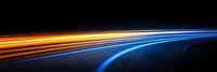 Abstract light trails in orange and blue colors against dark background, dynamic motion effect with curved lines showing speed and technology movement.