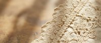 Delicate beige lace fabric with intricate floral patterns and scalloped edges on soft neutral background for wedding and fashion design projects.