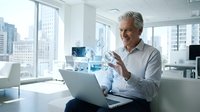 Mature Caucasian businessman using laptop with holographic digital interface technology in modern office workspace for business innovation and data analysis.