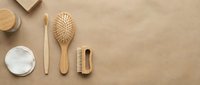 Eco-friendly bamboo personal care items including toothbrush, hair brush and comb arranged on natural beige background for sustainable lifestyle.