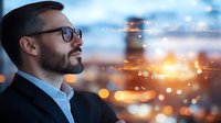 Professional middle eastern man with glasses and beard gazing thoughtfully at city lights and bokeh effect background, representing success, leadership and future vision.