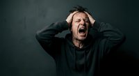 Stressed middle-aged Caucasian man screaming with hands on head expressing frustration, anxiety and mental breakdown against dark background.