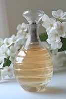 Elegant glass decanter with amber liquid and white jasmine flowers in soft focus background, luxury fragrance and cosmetic product styling for spa and beauty.