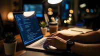 Software developer coding on laptop in modern office workspace with warm ambient lighting and bokeh background during evening work session.