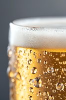 Close-up macro shot of fresh draft beer with bubbles and foam head against dark background, showing golden color and carbonation details in glass.