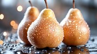 Fresh pears with water droplets on dark surface against blurred bokeh background, creating elegant food composition for culinary projects.